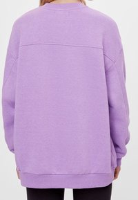Felpa viola con vestibilità rilassata, polsini e orlo a coste. Presenta una texture liscia e un dettaglio in cucitura sulla parte superiore della schiena.