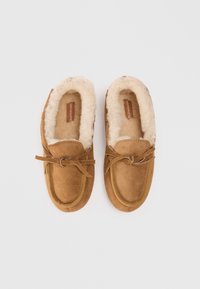 Brown suede moccasin slippers with plush cream lining, tied laces, and a rounded toe. Features a stitching detail along the edges.