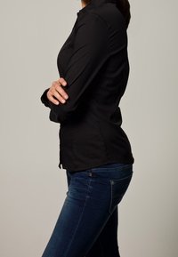Camicia nera a maniche lunghe con un design aderente, colletto button-down e tessuto liscio, abbinata a jeans in denim blu scuro.