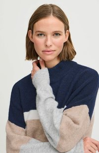 Pull rayé bleu marine, gris et beige fabriqué en matériau doux, avec un col montant et des poignets côtelés. Présente des blocs de couleur variés en lignes horizontales.