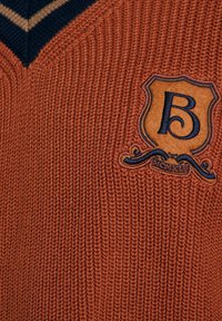 Sweter w kolorze rdzawym o głębokim dekolcie w kształcie litery V, z kontrastującymi granatowymi paskami oraz teksturowaną naszywką z wytłoczonym litera "B".