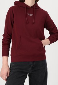 Felpa con cappuccio color bordeaux, dotata di tasca a marsupio, polsini a costine e un piccolo logo bianco sul petto. Materiale morbido in misto cotone.