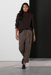 Brown knit turtleneck sweater with a V-neck, paired with high-waisted, pleated brown pinstripe trousers and shiny black loafers.