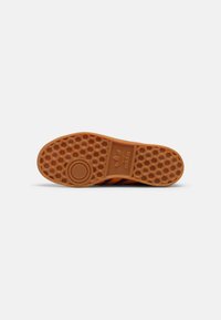 Shoe sole with a honeycomb texture, orange rubber material, featuring a circular logo and three purple stripes along the side.