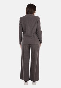 Completo grigio in velluto con giacca aderente e pantaloni a gamba larga. Il tessuto è morbido, senza cuciture e presenta una texture sottile. Nota per il suo design su misura.