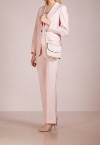 Lyserød skræddersyet jakkesæt med en enkelt knap, matchende høj talje bukser, og en lille hvid crossbody taske med guldfarvet hardware.