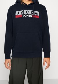 Felpa blu navy in misto cotone, con tasca a marsupio frontale e una grafica con logo "JACK & JONES" sul petto in rosso e bianco.