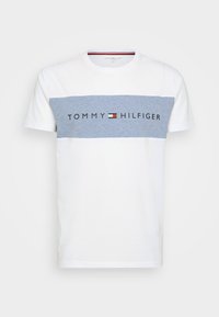 Bijela majica sivo prugasta, s natpisom "TOMMY HILFIGER" ispisanim crnom bojom. Okrugli izrez i kratki rukavi. Mekani pamučni materijal.