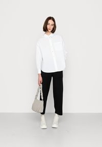 Fehér, oversized gombos ing, fekete, bő szárú nadrág, bézs táska texturált pánttal, és fehér bokacsizma. Egyszerű, modern dizájn.