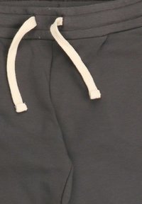 Dunkelgraue Jogginghose mit einem cremefarbenen, gefalteten Kordelzug, der durch einen gerippten, elastischen Bund gezogen ist.