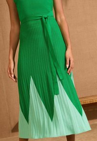 Abito in maglia con top verde aderente e gonna a campana con righe verticali, che sfuma dal verde scuro al verde menta chiaro con orlo a punta.