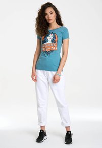Turquoise cotton t-shirt with a Wonder Woman graphic in orange, paired with white cropped pants and black sneakers. Smooth texture.