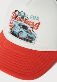 Fehér és piros sapka, amelyen egy hímzett kék versenyautó látható lángokkal, kockás zászlóval és a "New Era Racing" felirattal.