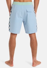 Světle modré plavky s mentolově zeleným pasem, s kostkovaným vzorem v tmavě modré barvě po stranách a zadní kapsou.