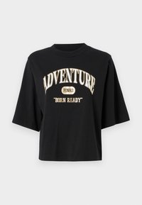Juodas medvilninis T-palaidinė su per didelėmis trumpomis rankovėmis. Priekyje yra balti ir auksiniai užrašai: "ADVENTURE PINKO 'BORN READY'".