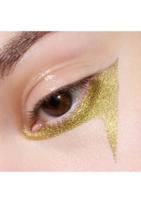 Fard à paupières doré appliqué en forme triangulaire autour de l'œil, contrastant avec une peau lisse et claire et un iris brun foncé.