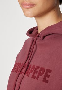 Felpa color marsala con cappuccio, caratterizzata da un cordino e da un grande logo del marchio tono su tono sul petto. Tessuto morbido e testurizzato con una vestibilità comoda.