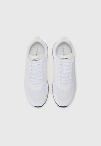 Scarpe sportive bianche con una tomaia in rete, lacci bianchi piatti e suola blu. Presentano il logo del marchio sulla linguetta e sul lato in rosso e blu navale.