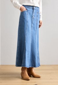 Denim maxi-rok in lichtblauw met een rechte snit, voorzien van voorzakken en een knoopsluiting, gecombineerd met tan enkellaarsjes.