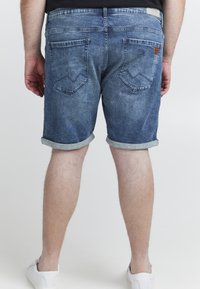 Denimshorts i mellemblå med et falmet look, opsmøg på kanten og to baglommer med en syet design og et lille lædermærke.