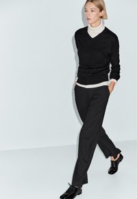 Maglione nero a V sovrapposto a un dolcevita bianco, pantaloni neri a vita alta e scarpe nere stringate. Design minimalista; texture liscia.