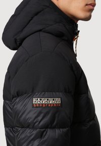 Sort pufferjakke med hætte, der har et syet mærke. Materialet er glat med en blank finish, der fremhæver de quiltede sektioner.