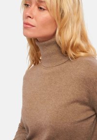 Hellbrauner Rollkragenpullover aus weichem, fein gestricktem Stoff. Hat ein tailliertes Design und einen gerippten Halsauschnitt, der eine glatte Textur bietet.