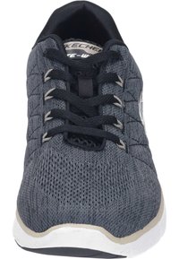 Zapatilla gris con un upper de tejido texturizado, cordones negros y una media suela blanca. Presenta áreas de malla transpirable para ventilación.