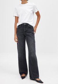 Black wide-leg jeans with a high waist, five pockets, and subtle whiskering. Paired with a plain white t-shirt and black pointed flats.