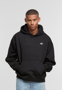 Black hooded sweatshirt featuring a front pocket and white "def" logo on the left chest. Fabric appears soft and textured.