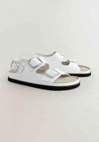 Sandali bianchi con due cinghie regolabili a fibbia argentata, soletta imbottita beige e suola in gomma nera. Materiale sintetico liscio.