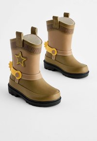 Bottes en caoutchouc marron avec une semelle noire, ornées d'une étoile et d'accents jaunes. Mise en valeur par une frange en faux cuir sur le bord supérieur.