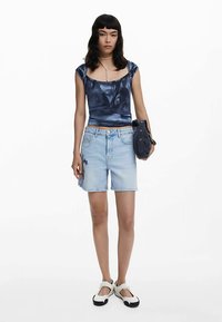 Sinine satiinist lühike top, hele sinised teksapüksid tikandiga ning must käekott. Jalanõud on valge põhjaga ja mustade detailidega.