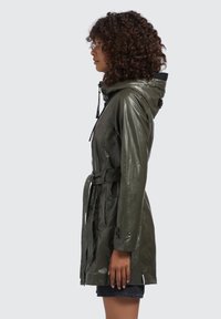 Waterdichte olijfgroene regenjas met een getailleerde taille en capuchon, voorzien van een glanzende afwerking, een trekkoord en geknoopte mouwen.