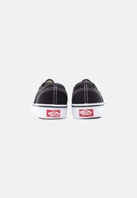 Μαύρα πάνινα παπούτσια χωρίς κορδόνια με λευκές λαστιχένιες σόλες και κόκκινες λεπτομέρειες με λογότυπο. Διαθέτουν αντίθετη λευκή ραφή και σιλουέτα χαμηλού προφίλ.