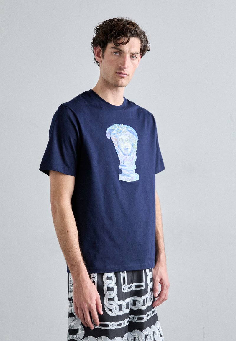 T-shirt en coton bleu marine avec un graphisme coloré d'un buste classique. Manches courtes et col rond. Modèle stylé avec un short à motifs.