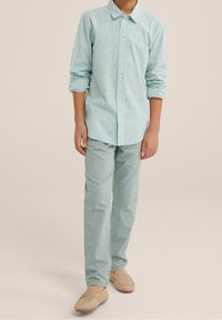 Světle modrá pruhovaná košile s dlouhým rukávem a malými zelenými akcenty, kombinovaná se světle modrými kalhotami a béžovými mokasíny. Hladká textura, ležérní střih.