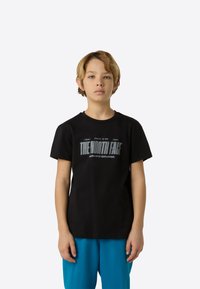 Fekete pamut póló, amelyen ezüstszínű "THE NORTH FACE" logó látható. Kék rövidnadrággal párosítva, a dizájn egyszerű és laza.