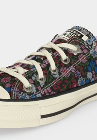 Κοντινή λήψη ενός αθλητικού παπουτσιού Converse με λευκά κορδόνια και πολύχρωμο λουλουδάτο μοτίβο πάνω στο υφασμάτινο επάνω μέρος.