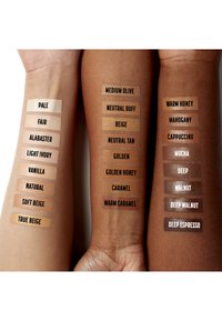Campioni di fondotinta in diverse tonalità su due braccia, etichettati con nomi come "Pallido," "Beige," "Mocha," e "Deep Espresso."