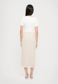Haut blanc à manches courtes associé à une longue jupe beige avec des motifs texturés verticaux et une taille ajustée.