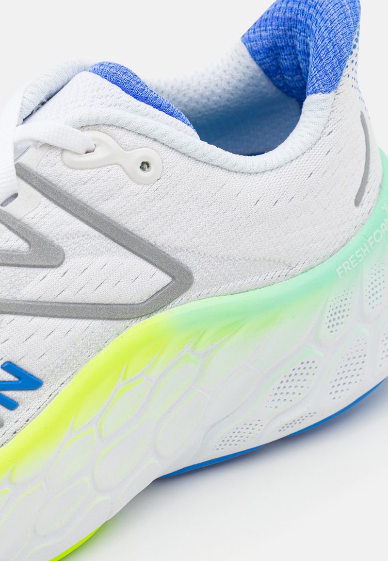 Zapatilla deportiva blanca con parte superior de malla, acentos azules en el cuello y una suela de gradiente multicolor con un patrón texturizado.