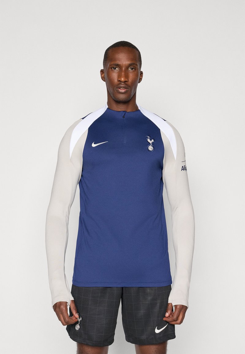 Navy blue athletic jersey with a high collar, white shoulder accents, and team logo; paired with black plaid shorts and Nike branding.