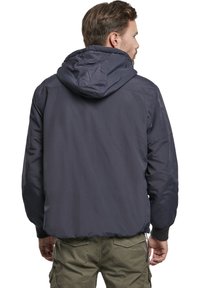 Chaqueta con capucha de color azul marino, de textura suave, con puños elásticos y capucha con cordón. Presenta un corte holgado y un diseño sencillo.