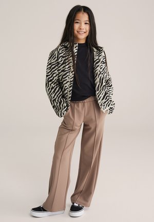 Zwart-wit jasje met zebrapatroon, zwart topje, beige wijde broekspijpen en zwarte sneakers met witte zolen. Gladde stoftextuur.