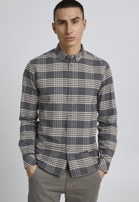 Grå rutete skjorte med lys beige og mørkegrå striper; har krage, lange ermer og en glatt tekstur.