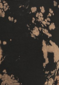 Svart bomulls tyg med ett batikmönster av ljusbruna fläckar, vilket skapar en oregelbunden design med varierande storlekar och former i hela tyget.