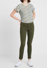 Květinový top s krátkým rukávem v světle modré barvě s mnohobarevnými vzory, spojený s olivově zelenými skinny džíny a bílými teniskami.