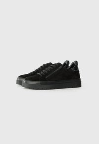 Adidași negri din suede cu o suprafață texturată, având șireturi în față și un fermoar lateral. Talpa este din cauciuc solid negru, cu striuri.