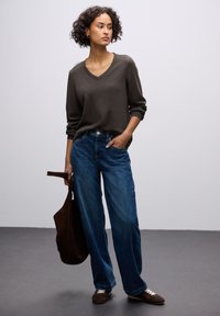Brauner V-Ausschnitt-Pullover, kombiniert mit locker sitzenden blauen Jeans. Eine braune Tasche und Schuhe ergänzen den lässigen Look. Glatte Textur.